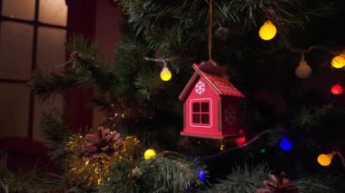 Kar tanesi detaylarıyla dolu kırmızı ahşap bir ev süsü güzel dekore edilmiş bir Noel ağacına asılı renkli parlak ışıklar ve şenlikli çam dallarıyla