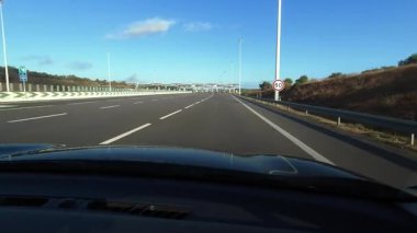 Birinci şahıs sürücünün bakış açısı modern Portekiz otoyol gişelerinden geçişi gösteriyor. Birden fazla şeridi, yeşil şeritleri ve güneşli yol gezisi sırasında yakalanan tepe örtüleri var.