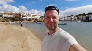 Gezgin, geleneksel beyaz binaları, limandaki küçük balıkçı tekneleri ve yaz tatili anıları için mükemmel mavi gökyüzü olan büyüleyici Portekiz kıyı kasabasının arka planında unutulmaz bir selfie anı yakalıyor.