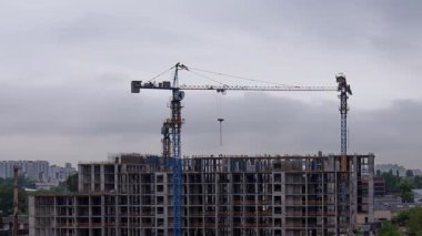 Şehir ortamında yerleşim kompleksinde çalışan vinçlerin zamanlanmış görüntüleri, çok katlı bir apartman yapısı inşa eden vinçlerle modern mülk inşaatının dinamik sürecini gösteriyor.