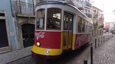 Lizbon, Portekiz - 14 Ekim 2019 Coca-Cola reklamlı klasik kırmızı ve sarı tramvay Lizbon 'un tarihi bölgesinde dar kaldırım taşı caddesinde dekoratif ön cepheleri ve balkonları olan geleneksel Portekiz binalarıyla çevrili.