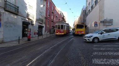 Lizbon, Portekiz - 10 Ekim 2019: Lizbon 'da tarihi Portekiz binalarıyla dar kaldırım taşları caddesinde yürüyen ikonik kırmızı ve sarı klasik tramvay, şehrin geleneksel ulaşım sistemini yakalayan mükemmel şehir manzarası yaratıyor.