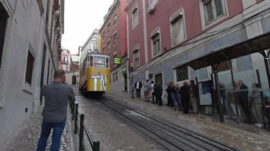 Lizbon, Portekiz - 9 Ekim 2019: Lizbon 'da geleneksel Portekiz mimarisi tarafından çevrelenmiş dik kaldırım taşı caddesine tırmanan tarihi sarı füniküler tramvay turistler ve yerel halk için benzersiz kentsel ulaşım deneyimi sunuyor