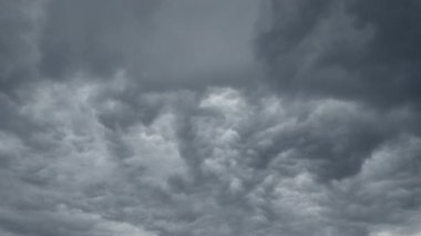 Dramatik gri bulutlar bulutlu gökyüzünde sürükleniyor büyüleyici zamanlamayla, doğanın dinamik hava modellerini ve atmosferik hareketlerini sinematik detaylarla gösteriyor.