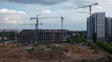 Sabit mavi vinçlerle kentsel inşaat alanının zaman çizelgesi ve bitmemiş konut binalarının üzerinde hareket eden bulutlar, hareketsiz inşaat ekipmanları ve dinamik gökyüzü arasındaki karşıtlığı gösteriyor