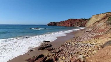 Gök mavisi okyanus dalgalarının büyüleyici görüntüsü, Portekiz 'in batısındaki Algarve kıyıları boyunca uzanan belirgin kızıl kayalıklarla çevrili altın kumlu plajlara doğru yavaşça süzülüyor.