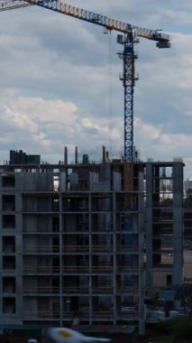 Kule vinci bulutlu gökyüzünün altında beton bina iskeleti inşa ediyor. Lüks konut yatırımları ve ev sahipliği hayalleri için emlak geliştirme sürecini gösteriyor.