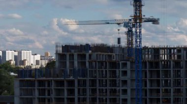 Kule vinci, inşaat malzemelerini, açık mavi gökyüzü altında, yatay zaman aralığında beyaz bulutlar bulunan apartman kompleksi inşa eden işçilere teslim ediyor.