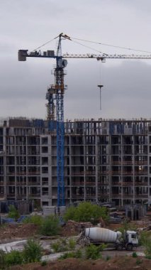 Mavi kule vinçlerinin dikey görüntüsü, çok katlı bir konut kompleksi inşa ederken görülebilir beton iskeleti, modern kentsel gelişim ve inşaat ekipmanlarını ön planda çimento karıştırıcı da dahil olmak üzere sergiliyor