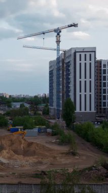 Gündüz koşullarında dinamik bir gökyüzüne karşı kentsel gelişimi gösteren, arka planda hızla hareket eden bulutlar olan modern bir apartmanın yanında durağan bir inşaat vincinin yer aldığı zaman aralığı.