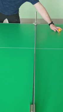 Masa tenisçisi, profesyonel yeşil kortta oynanan kapalı alanda oynanan spor müsabakasında rakip oyuncuya sarı ping pong topu atıyor.