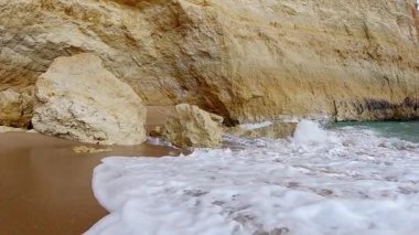 Portekiz 'in Algarve bölgesindeki Benagil Sahili' nin altın kumları üzerinde, dünyaca ünlü Benagil Mağarası 'nın yakınında hafif Atlantik dalgalarının büyüleyici yavaş çekim görüntüleri. Kristal berrak turkuaz sular barışçıl bir ritim yaratır.