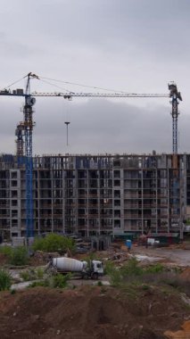 Dikey zaman dilimi görüntüleri apartman inşaatını gösteriyor. Dönen vinçler ve bitmemiş katlarda hareket eden işçiler kentsel kalkınma bölgesindeki dinamik yapı sürecini belgeliyor.