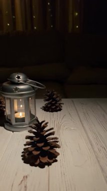  Parlayan metal bir fener ve yanan bir mum, çam kozalaklarıyla çevrili ahşap bir masada oturur. Video, sağdan sola bir kamera hareketi yakalıyor ve rahat bir atmosfer yaratıyor.