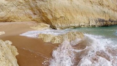 Kristal berrak Atlantik dalgalarının büyüleyici yavaş çekim görüntüleri Portekiz 'deki güzel Algarve plajında altın kumun üzerinde yavaşça akıyor.