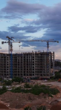 İnşaat sürecini gösteren bir inşaat alanının dikey zaman çizelgesi. Vinçler şehrin dramatik bir günbatımı gökyüzü altında modern yapıda çalışırlar.