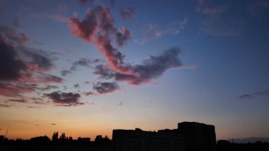 Şehir siluetinin üzerinde sakin bir günbatımı zamanı var. Güzel, renkli gökyüzünü izleyin akşam bulutları yavaşça kaybolurken