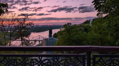 Kyiv 'de gün doğumunda Dnipro nehri, yaya köprüsü, St Volodymyr anıtı ve yemyeşil, el kamerası yavaşça tırabzana yaklaşıyor.