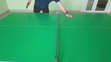 Masa tenisçisi, profesyonel yeşil kortta oynanan kapalı alanda oynanan spor müsabakasında rakip oyuncuya sarı ping pong topu atıyor.