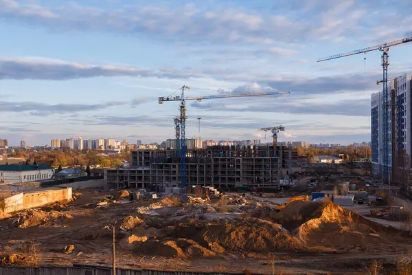 Akşam gökyüzü altında vinçleri, makineleri ve binaları olan kentsel inşaat alanı, şehir gelişimini, takım çalışmasını ve modern mimari ilerlemesini gösteriyor