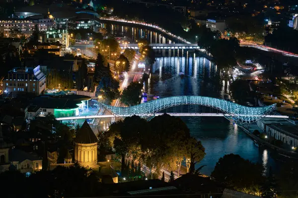 Barış Köprüsü, Tiflis Gürcistan 'daki Kura Nehri üzerinde gece aydınlandı, modern mimari, şehir simgesi, yansıma, turizm, manzaralı şehir manzarası, seyahat, gece manzarası