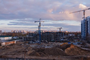 Günbatımında vinçleri ve ağır makineleri olan kentsel inşaat alanı dramatik akşam gökyüzü altında şehir gelişimini, takım çalışmasını ve modern mimari ilerlemesini gösteriyor.