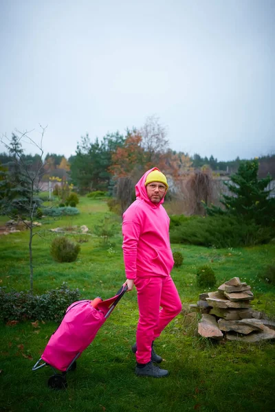 Pink man posing outdoor in pink sport suit with rolling bag.