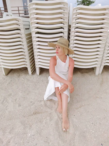 藁帽子をかぶった若い女性のファッションの肖像 コピースペースとビーチに座って官能的な女の子 魅力的な女の子見ますカメラ — ストック写真
