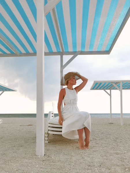 白いドレスと夏の帽子を身に着けている空のビーチでブロンド若い女性の肖像 — ストック写真