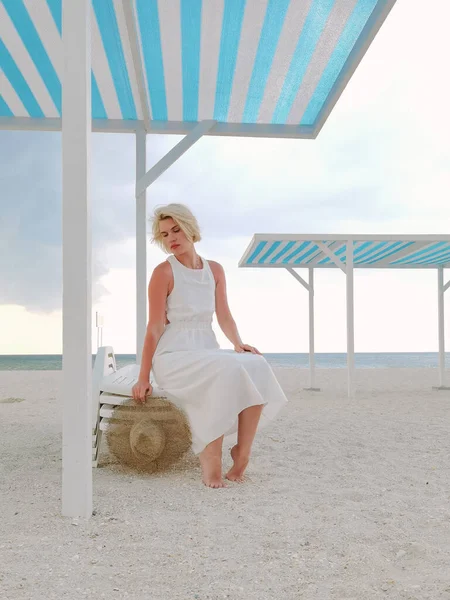 白いドレスと夏の帽子を身に着けている空のビーチでブロンド若い女性の肖像 — ストック写真