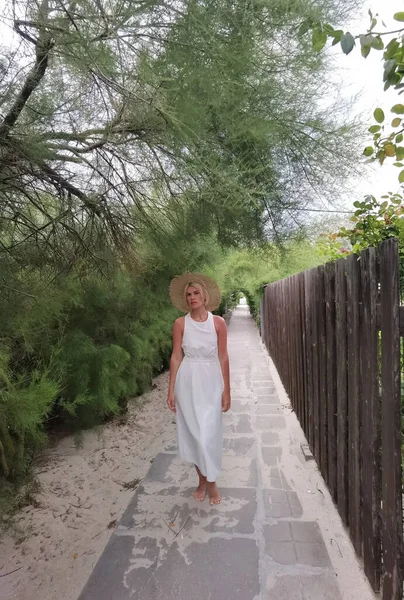 穿着白色夏装的年轻漂亮的时髦姑娘在小巷的树间散步和摆姿势 — 图库照片