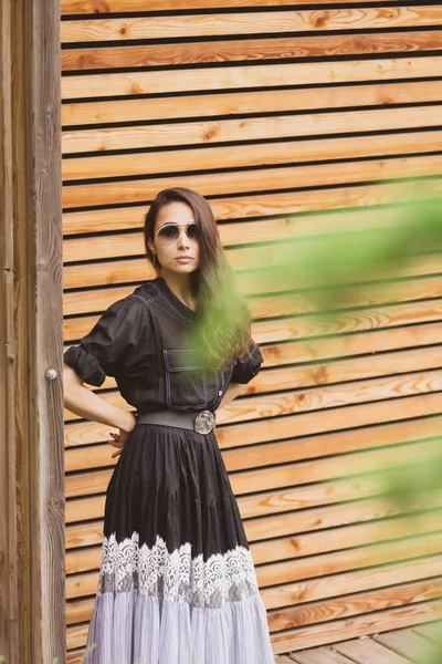 流行の服を着て 通りに立って若いスタイリッシュなヒップスター女性のライフスタイルファッションの肖像画 黒のドレス 木の背景 — ストック写真
