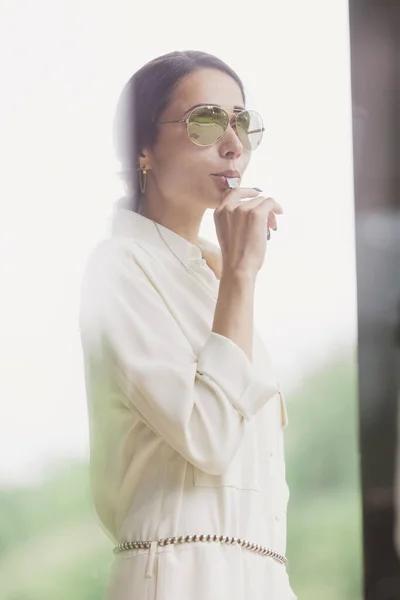 stock image Portrait of attractive brunette holding whistle in her hand. Fashionable young woman with long hair in white costume standing in interior. Fan, coach, counselor