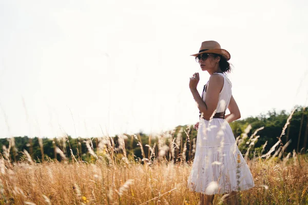 夏の牧草地で藁帽子とリネンのドレスを着て高い草の間を歩く若い女性の肖像画は自然を楽しんでいます 調和と均衡 — ストック写真