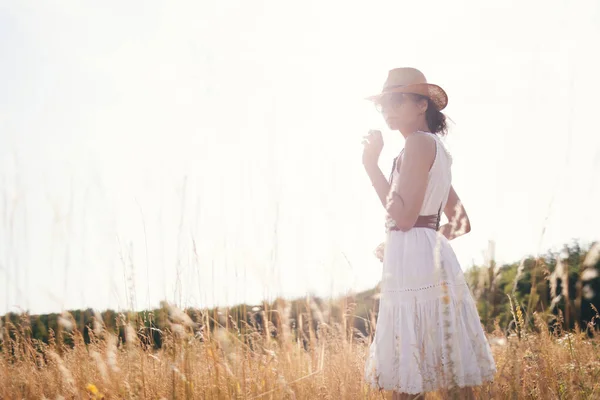 夏の牧草地で藁帽子とリネンのドレスを着て高い草の間を歩く若い女性の肖像画は自然を楽しんでいます 調和と均衡 — ストック写真