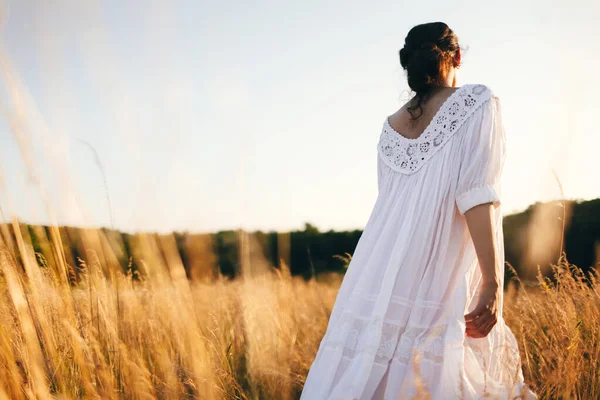 Brunette young woman in wild field. Natural beauty and romance concept. Sunset light. View from the back.
