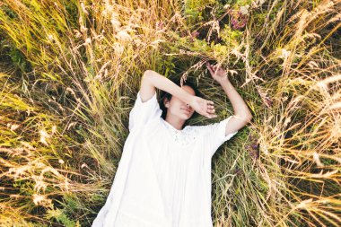 Beyaz bir elbise giymiş, çimenlerin üzerinde yatan hamile bir genç kadın. Doğa, yaz tatili, tatil ve insanlar konsepti