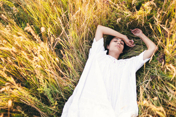 Conceived Beautiful young woman lying in the grass, wearing a white dress. Nature, summer holidays, vacation and people concept
