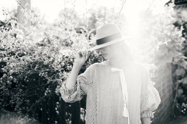 Romantik giyinmiş genç yetişkin güzel bir kadın kırsal bir parkta dinleniyor ve başka tarafa bakıyor. Beyaz şeffaf elbisesi ve hasır şapkasıyla bahçede yürüyen sarışın Paris tarzı bir model..