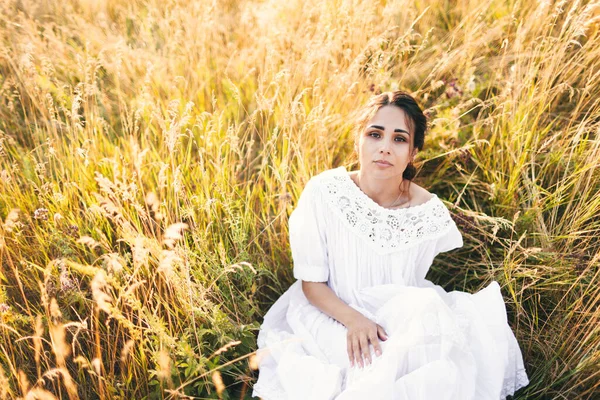 日落时穿着白衣的漂亮姑娘坐在麦田里 — 图库照片