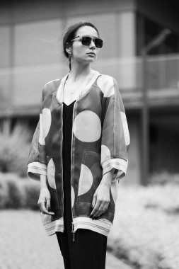 Açık havada poz veren siyah tulumlu güzel esmer kadın. Sokak modası. Şık kıyafet.