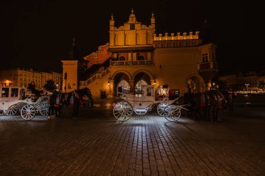 Krakow, Polonya - 24 Mayıs 2023: Eski şehir meydanındaki Mariacki katedralinin arka planında turistlere yönelik at arabaları.