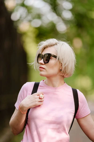 美丽时髦的年轻女子在公园里摆姿势 太阳镜 短短的金发 时尚夏季照片 明亮的颜色 风景不错 — 图库照片