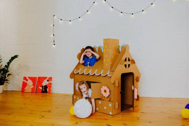 Neşeli kardeşler birbirlerini kovalayıp karton evin etrafında koşuşturuyorlar.