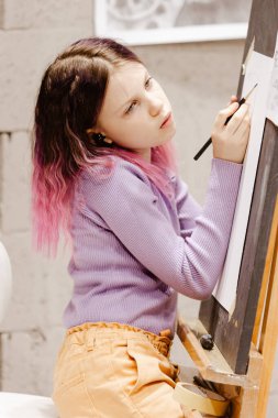 11 yaşındaki bir kadın stüdyoda resim yapıyor. Şövalenin önünde duruyor. Resim dersinde resim yapan bir kızın portresi.