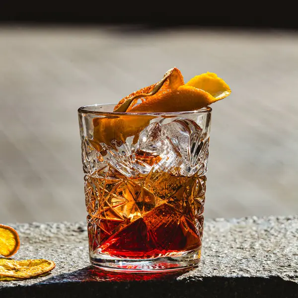 Delicious old fashion cocktail in the etched glass with ice and orange slices, dark wooden background. Shallow dof