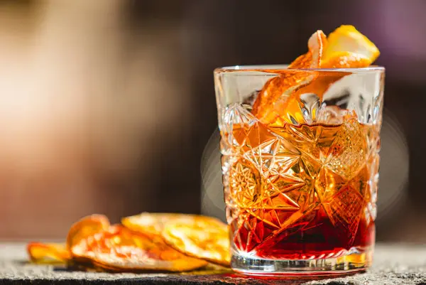 Delicious old fashion cocktail in the etched glass with ice and orange slices, dark wooden background. Shallow dof