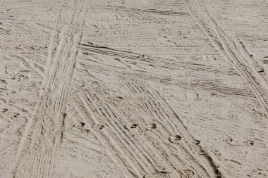 Kumlu bir yüzeye yerleştirilmiş lastik izlerinin detaylı görüntüsü. Görüntü, lastikler tarafından oluşturulan karmaşık desenleri ve dokuları ön plana çıkararak, açık hava faaliyetleri, kırsal alanlar ve doğal arka planlar ile ilgili projelerde kullanılmak için ideal hale getiriyor.