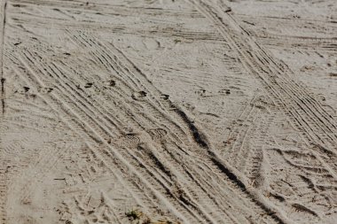 Kumlu bir yüzeye yerleştirilmiş lastik izlerinin detaylı görüntüsü. Görüntü, lastikler tarafından oluşturulan karmaşık desenleri ve dokuları ön plana çıkararak, açık hava faaliyetleri, kırsal alanlar ve doğal arka planlar ile ilgili projelerde kullanılmak için ideal hale getiriyor.