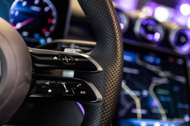 Kontrol düğmeleri ve parlak deri detayları olan lüks bir direksiyon simidinin yakın plan çekimi, yüksek teknolojili bir gösterge paneli ve navigasyon ekranı içeriyor..